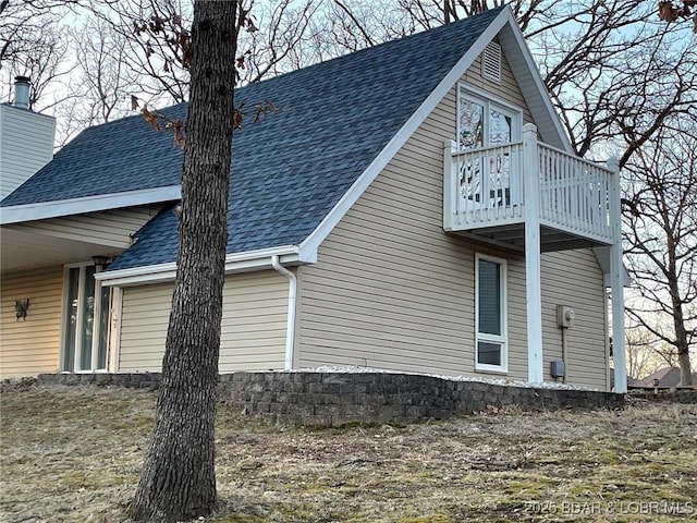 view of home's exterior with a balcony, roof with shingles, and a chimney