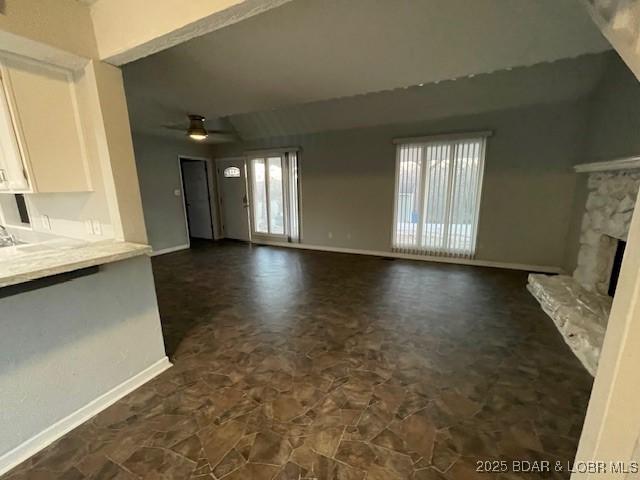 unfurnished living room featuring baseboards, a stone fireplace, and ceiling fan