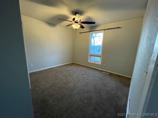 unfurnished room featuring visible vents, dark carpet, baseboards, and ceiling fan