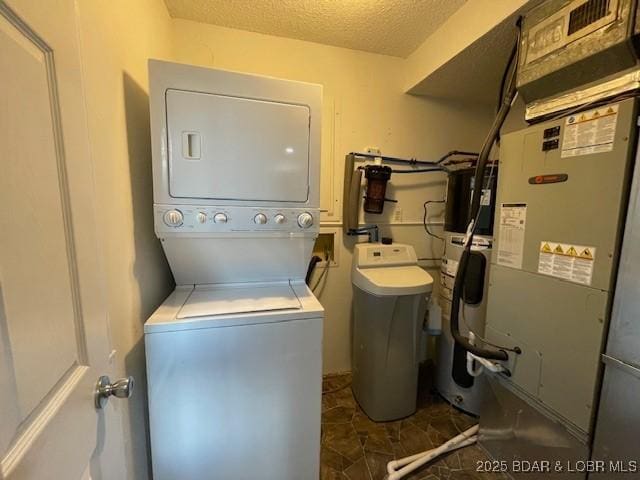 washroom with a textured ceiling, laundry area, heating unit, and stacked washing maching and dryer