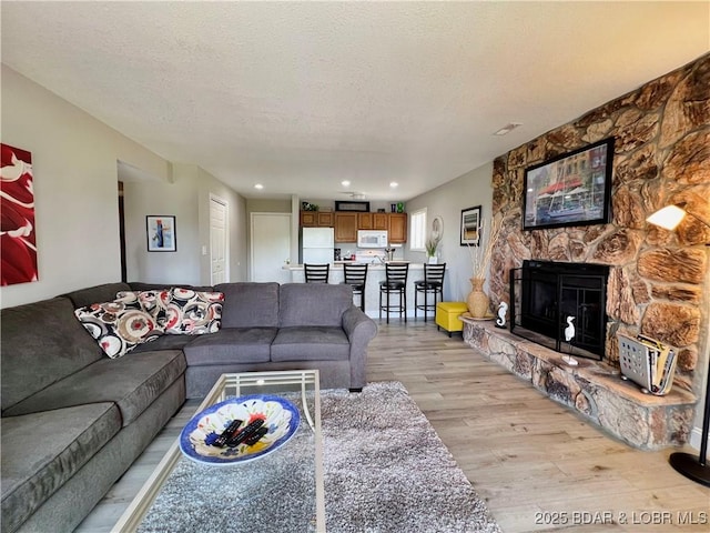 living area with recessed lighting, a stone fireplace, light wood-style flooring, and a textured ceiling