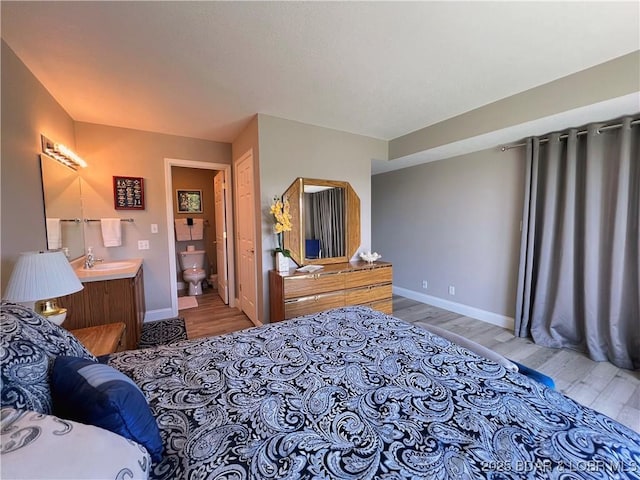 bedroom with ensuite bath, wood finished floors, baseboards, and a sink