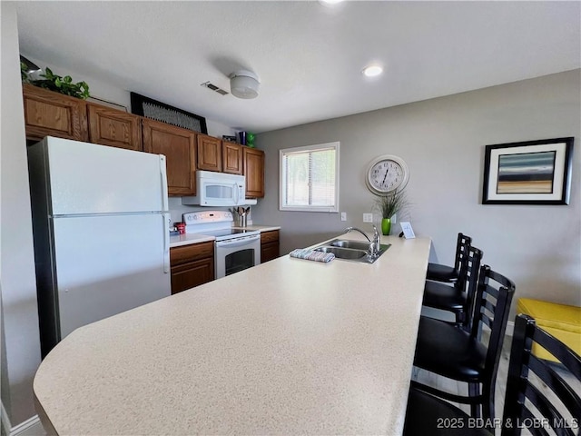 kitchen featuring a sink, a kitchen breakfast bar, white appliances, a peninsula, and light countertops