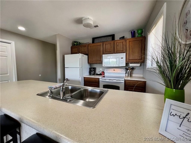 kitchen featuring light countertops, a kitchen bar, brown cabinetry, white appliances, and a sink