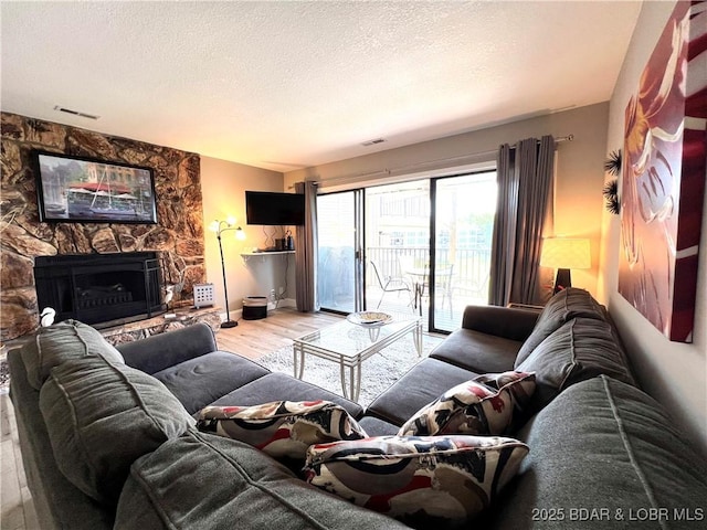 living room featuring visible vents, a textured ceiling, wood finished floors, and a fireplace