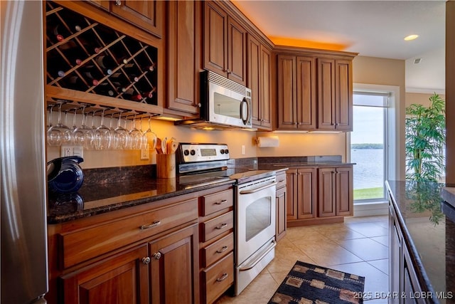 kitchen featuring light tile patterned floors, appliances with stainless steel finishes, dark stone counters, and brown cabinetry