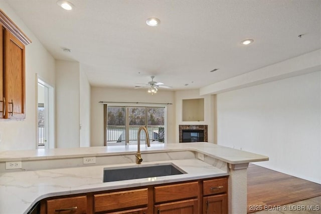 kitchen with brown cabinetry, recessed lighting, light stone counters, and a sink