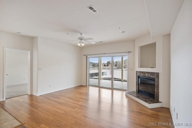 unfurnished living room featuring baseboards, visible vents, light wood-style flooring, a high end fireplace, and ceiling fan