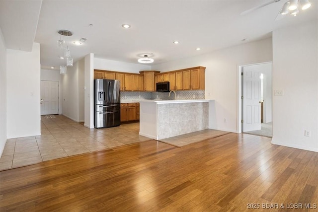 kitchen with stainless steel fridge, a peninsula, black microwave, light wood finished floors, and light countertops