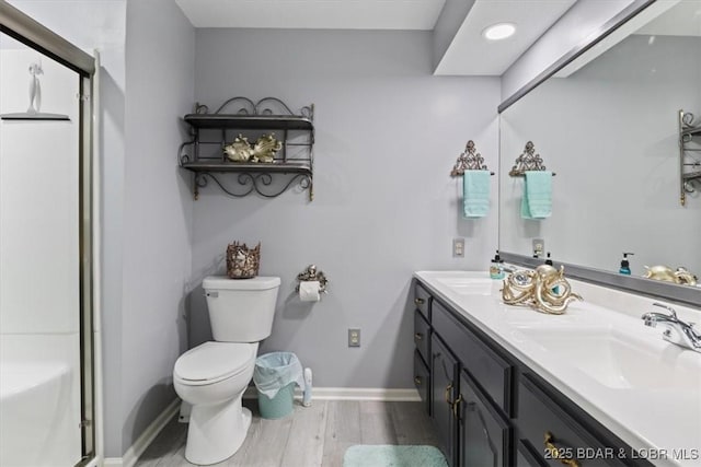 full bath featuring wood finished floors, baseboards, a shower with shower door, a sink, and toilet