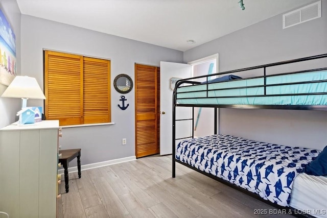 bedroom with visible vents, baseboards, two closets, and wood finished floors