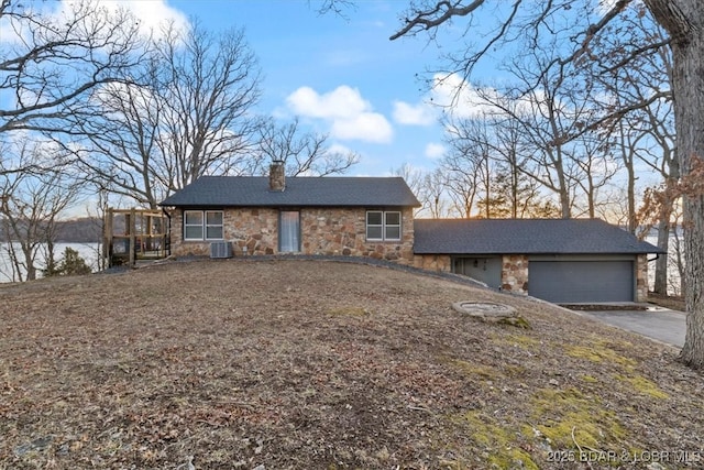 view of front of property featuring cooling unit, driveway, an attached garage, a chimney, and stone siding