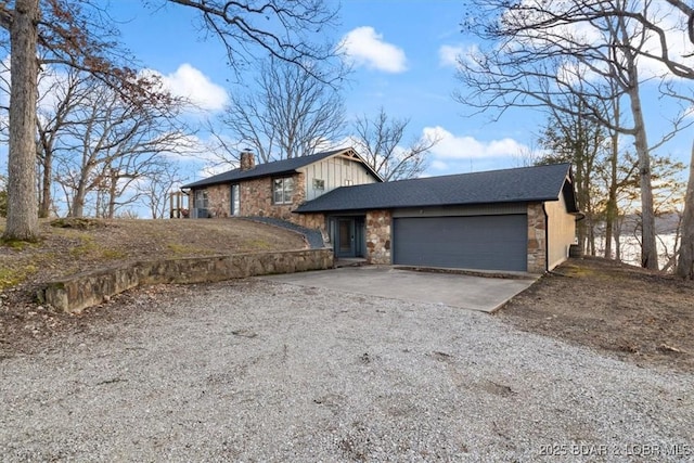 view of front of home with stone siding, a chimney, gravel driveway, and a garage