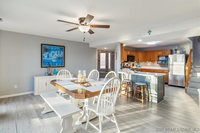 dining space featuring baseboards, a ceiling fan, light wood-style flooring, and stairs