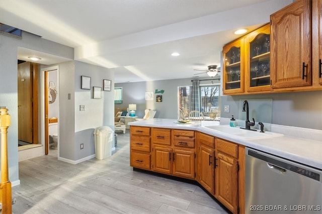 kitchen with a peninsula, a sink, light countertops, glass insert cabinets, and dishwasher