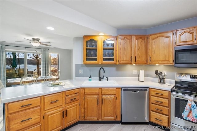 kitchen with a sink, glass insert cabinets, appliances with stainless steel finishes, and light countertops