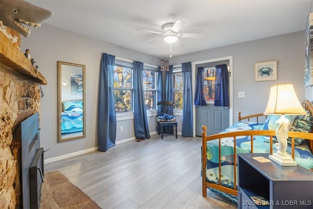 living room featuring light wood finished floors, a fireplace, baseboards, and ceiling fan