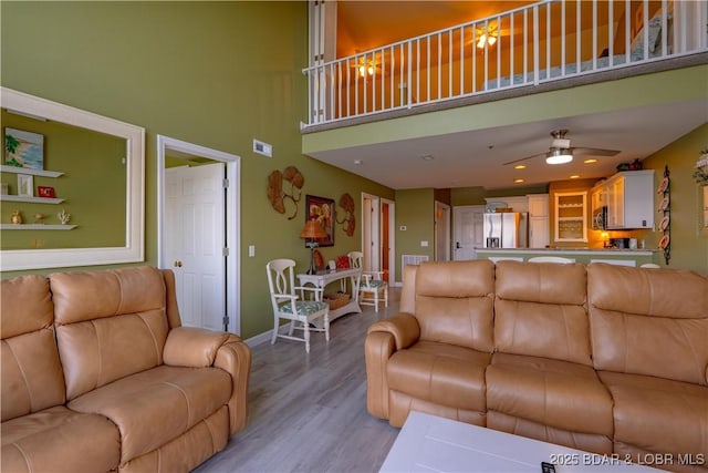 living room with visible vents, light wood-style flooring, a towering ceiling, baseboards, and ceiling fan