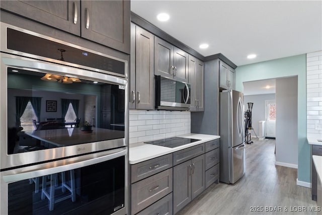 kitchen with gray cabinetry, light countertops, light wood-style floors, appliances with stainless steel finishes, and tasteful backsplash