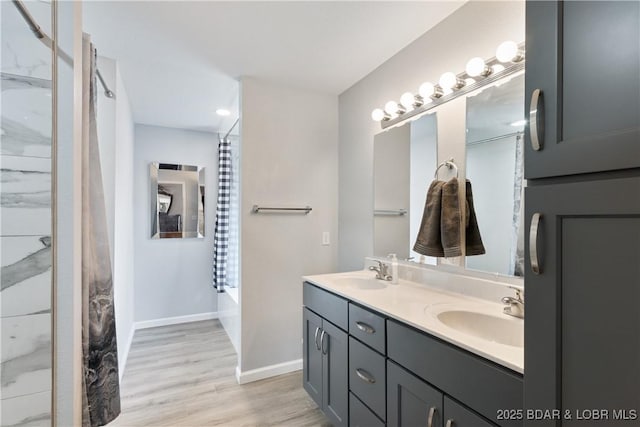 bathroom featuring double vanity, wood finished floors, baseboards, and a sink