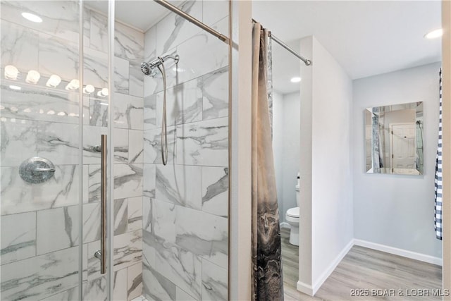 bathroom with wood finished floors, toilet, baseboards, and a stall shower