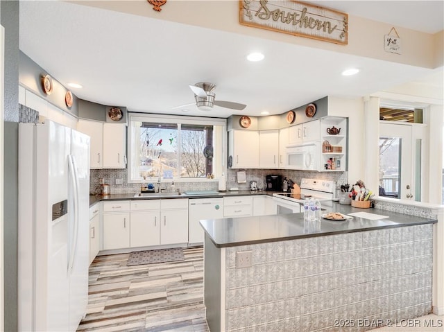 kitchen with dark countertops, backsplash, a peninsula, white cabinets, and white appliances