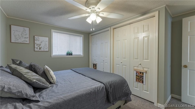 carpeted bedroom featuring two closets, ornamental molding, a textured ceiling, baseboards, and ceiling fan