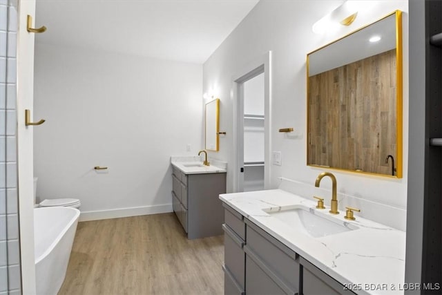 bathroom featuring wood finished floors, two vanities, baseboards, and a sink