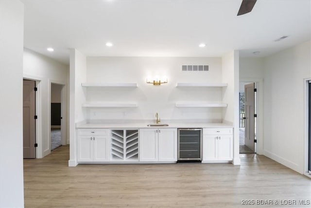 bar with visible vents, light wood-type flooring, a sink, wine cooler, and indoor wet bar