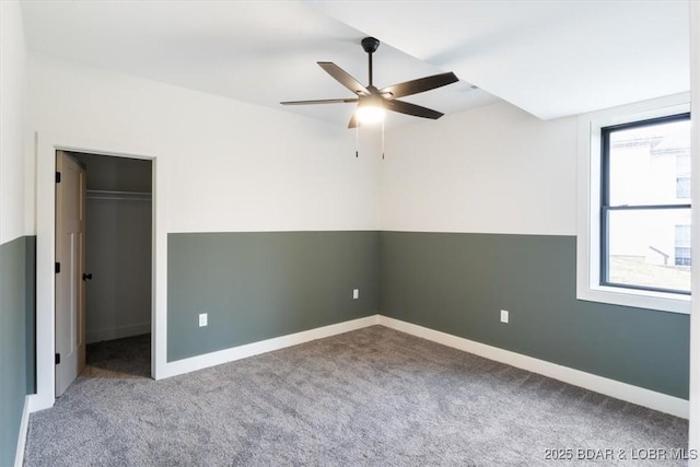 unfurnished bedroom with carpet flooring, ceiling fan, a walk in closet, and baseboards