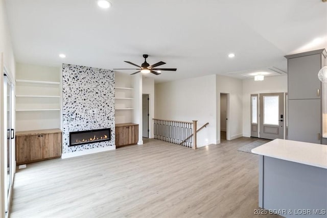 living room with light wood finished floors, recessed lighting, a warm lit fireplace, and ceiling fan