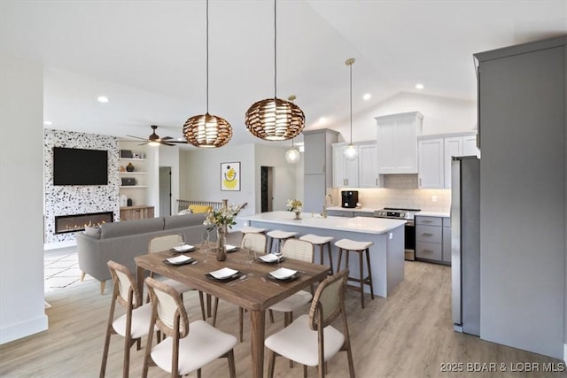 dining space featuring built in shelves, a large fireplace, lofted ceiling, and light wood-style flooring