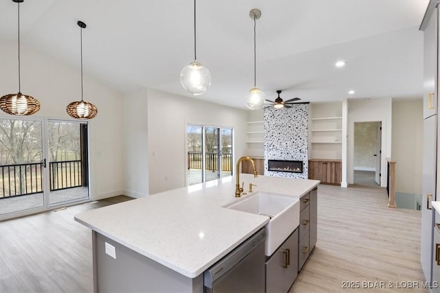 kitchen featuring a sink, light wood-style floors, stainless steel dishwasher, open floor plan, and a large fireplace