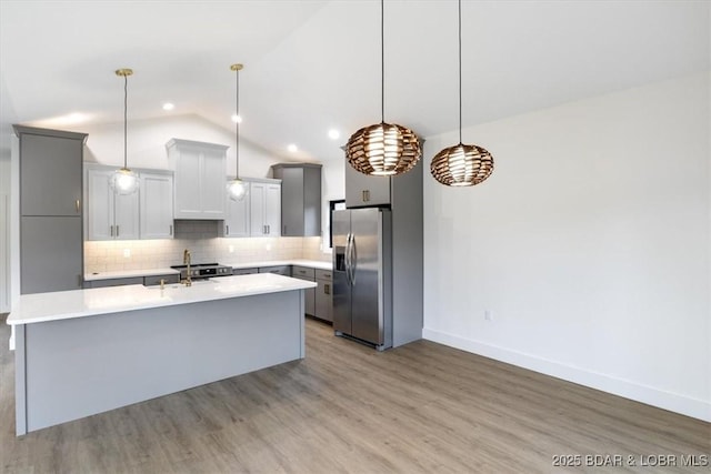 kitchen featuring lofted ceiling, stainless steel fridge with ice dispenser, light countertops, light wood-style floors, and tasteful backsplash