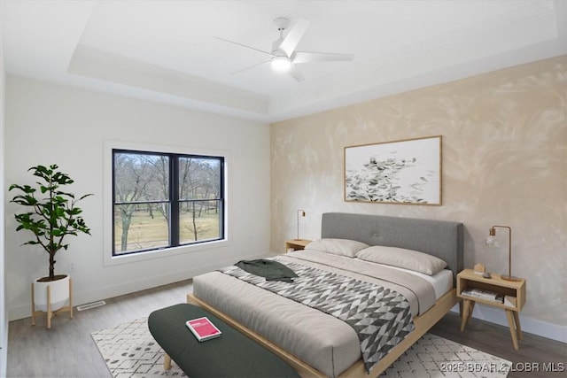 bedroom featuring a ceiling fan, a raised ceiling, light wood-style floors, and baseboards