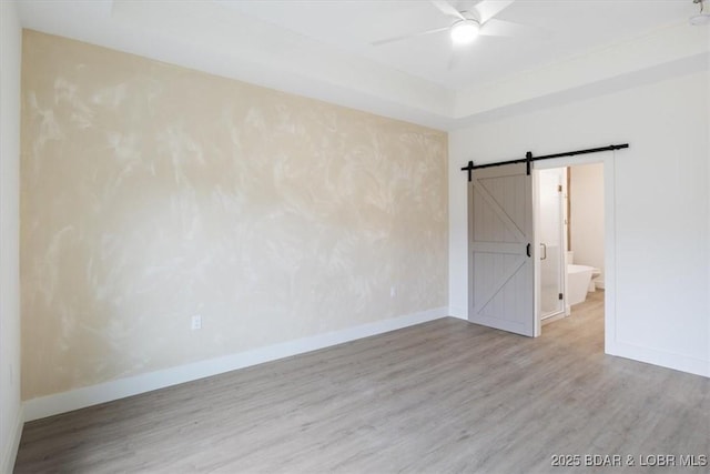 unfurnished room with a barn door, baseboards, and wood finished floors