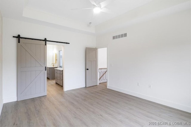 unfurnished bedroom featuring baseboards, visible vents, light wood finished floors, a tray ceiling, and a barn door