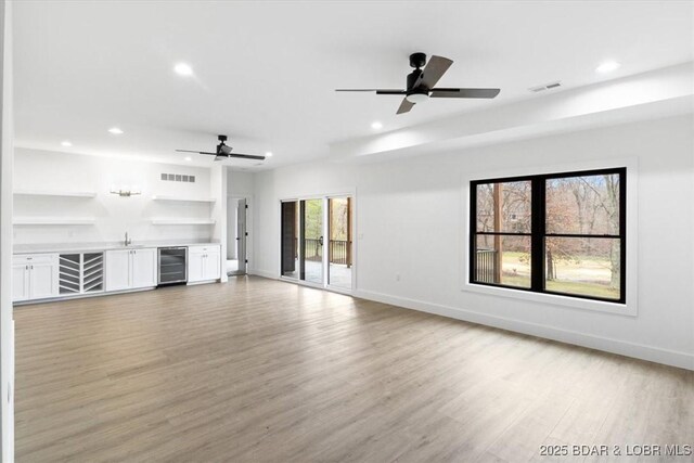 unfurnished living room with wet bar, light wood-style floors, beverage cooler, and visible vents