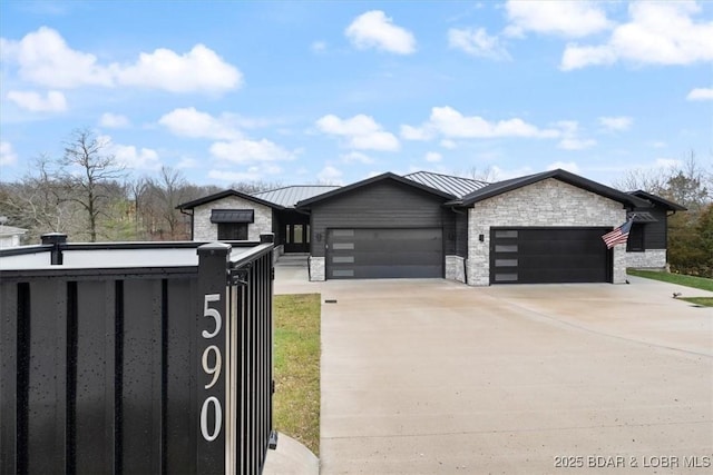 view of front facade with a standing seam roof, stone siding, metal roof, concrete driveway, and a garage