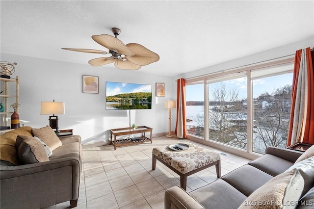 living area with light tile patterned floors, a ceiling fan, baseboards, and a textured ceiling