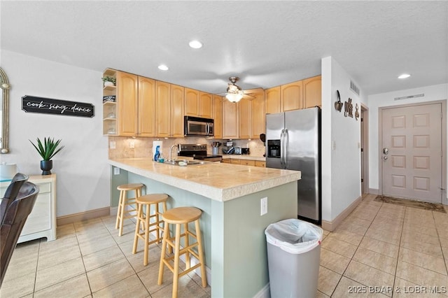 kitchen with a breakfast bar, light brown cabinetry, stainless steel appliances, a peninsula, and light tile patterned floors