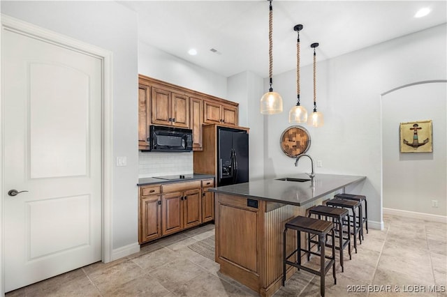 kitchen with a sink, black appliances, a kitchen bar, dark countertops, and brown cabinets