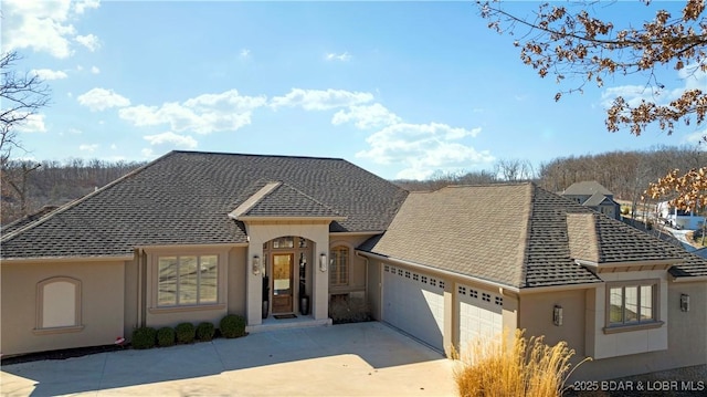 view of front facade featuring stucco siding, driveway, a garage, and roof with shingles