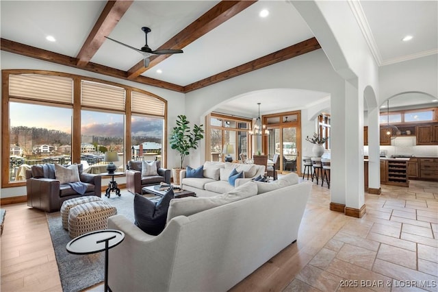 living area with beverage cooler, beamed ceiling, ceiling fan with notable chandelier, and baseboards