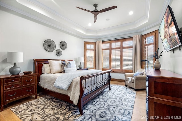 bedroom with light wood-style flooring, a raised ceiling, a ceiling fan, and ornamental molding