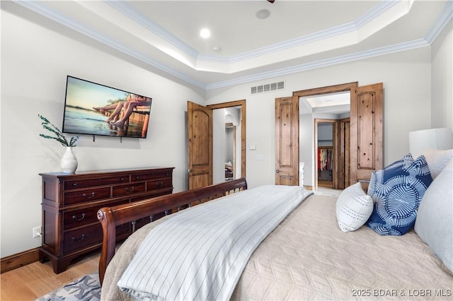 bedroom with baseboards, visible vents, a tray ceiling, crown molding, and light wood-type flooring