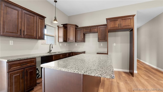 kitchen with baseboards, decorative light fixtures, light wood-type flooring, light stone counters, and a sink