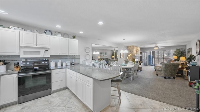 kitchen featuring white microwave, backsplash, a breakfast bar area, a peninsula, and electric range