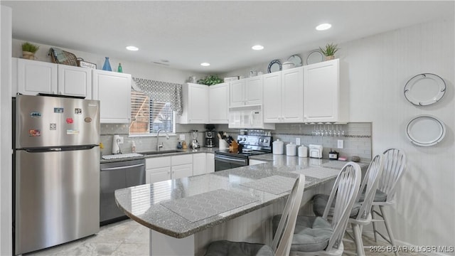 kitchen with a sink, a kitchen breakfast bar, stainless steel appliances, a peninsula, and white cabinets