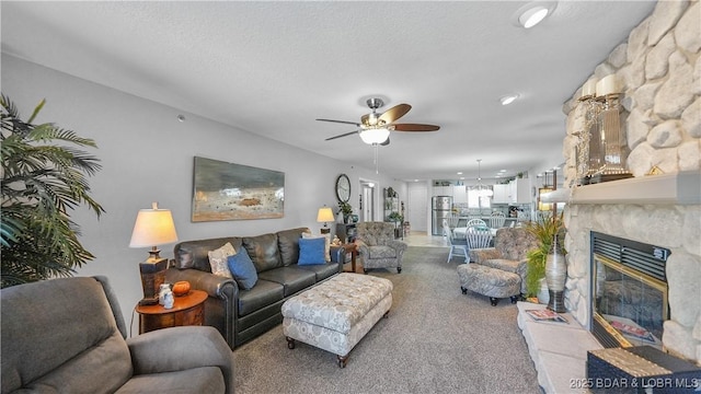 living room featuring ceiling fan, light colored carpet, a glass covered fireplace, and a textured ceiling